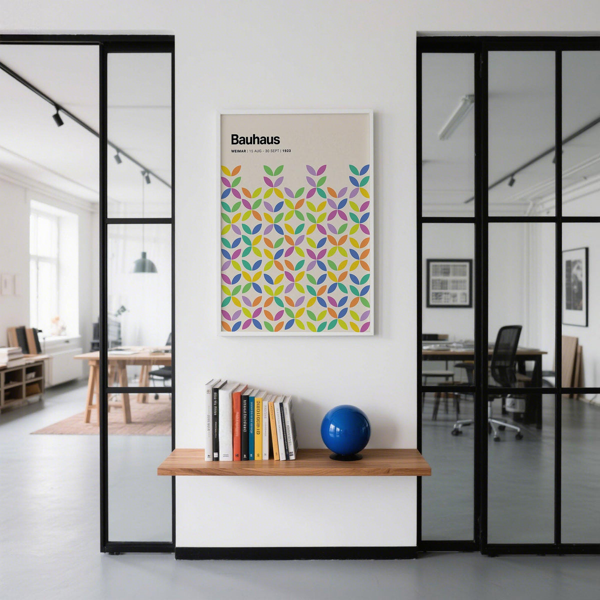 Colourful Bauhaus poster with abstract petals in multiple colours on an office wall above a shelf with books and a blue orb