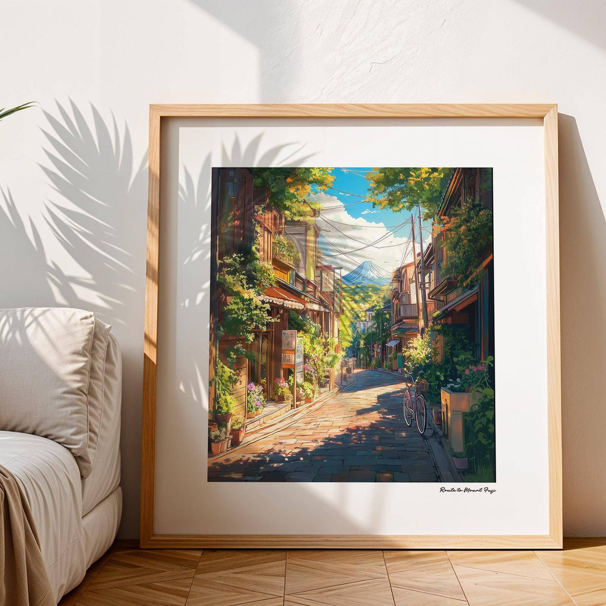 Framed print of a mountain street view with blue sky and green trees leaning on a wooden floor by a sofa