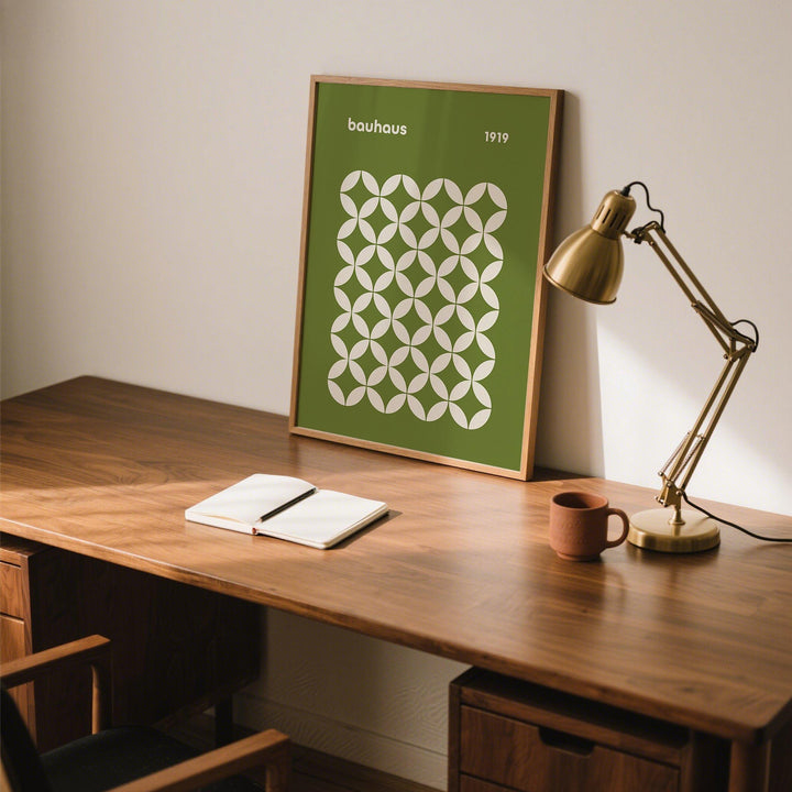Mid Century Geometric Bauhaus framed print with white circle petal pattern on green leaning on a desk next to a brass lamp
