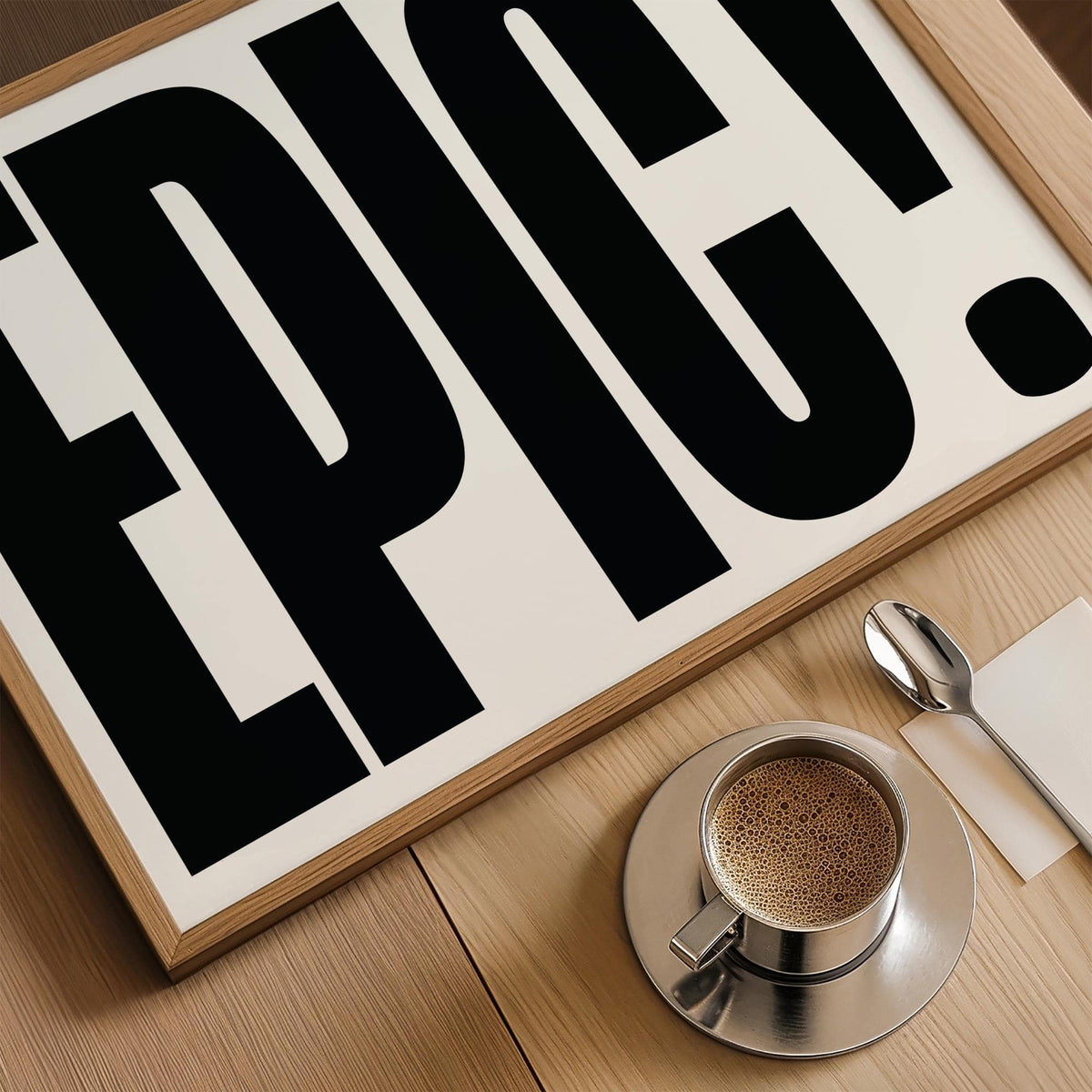 Close-up of Big Text Sign Wall Art with black EPIC typography and wooden frame on a wooden surface next to a coffee cup