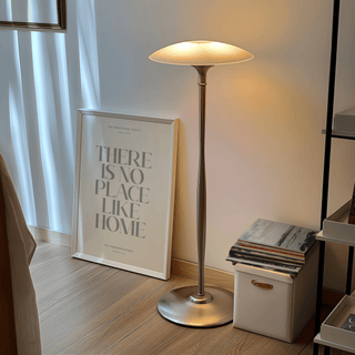 No Place Like Home print leaning on wooden floor near a lit silver floor lamp and small storage box