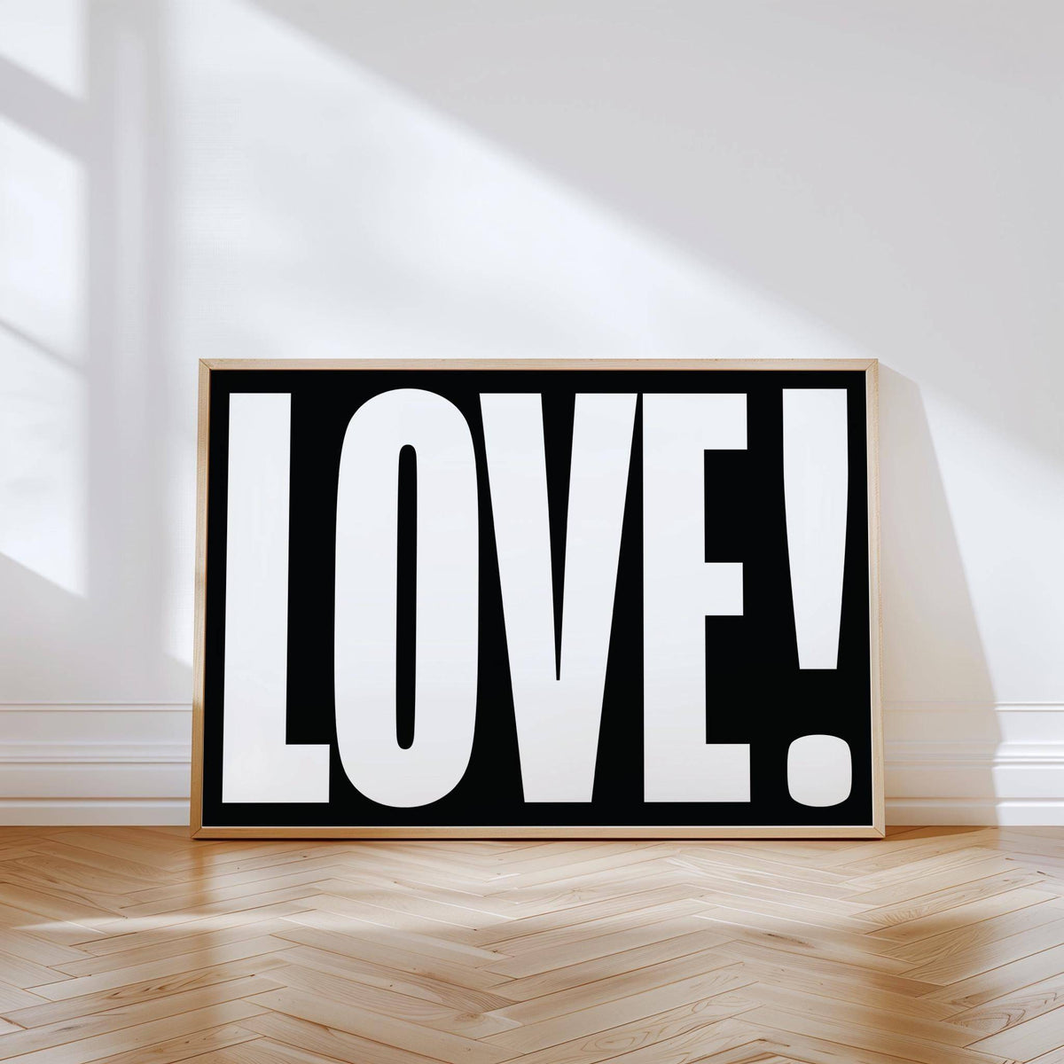 Print leaning on a floor with LOVE typography in white on black and a wooden frame with sunlight on the wall