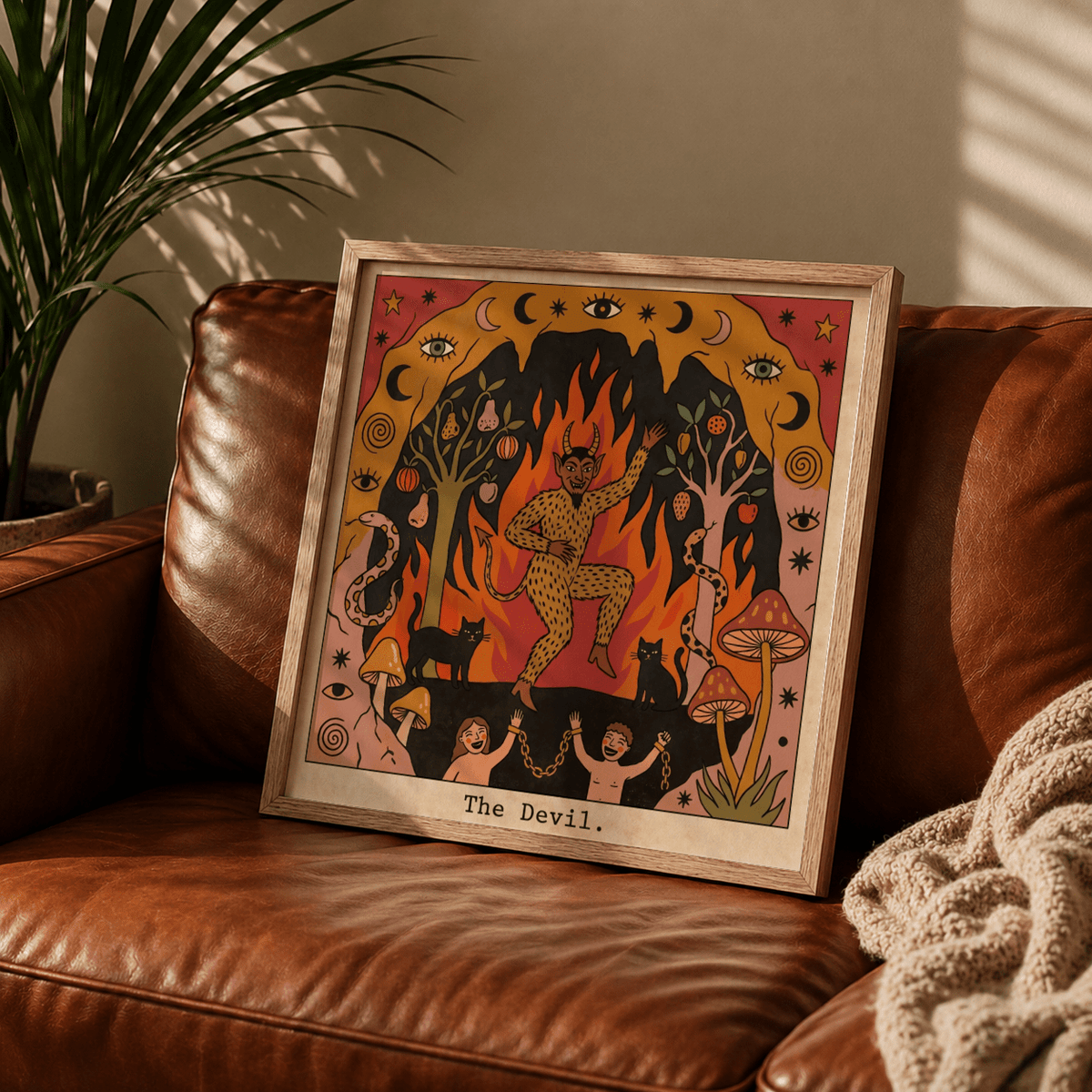 Framed print of The Devil Tarot Card Art with a dancing devil and folk-art style on a brown leather sofa