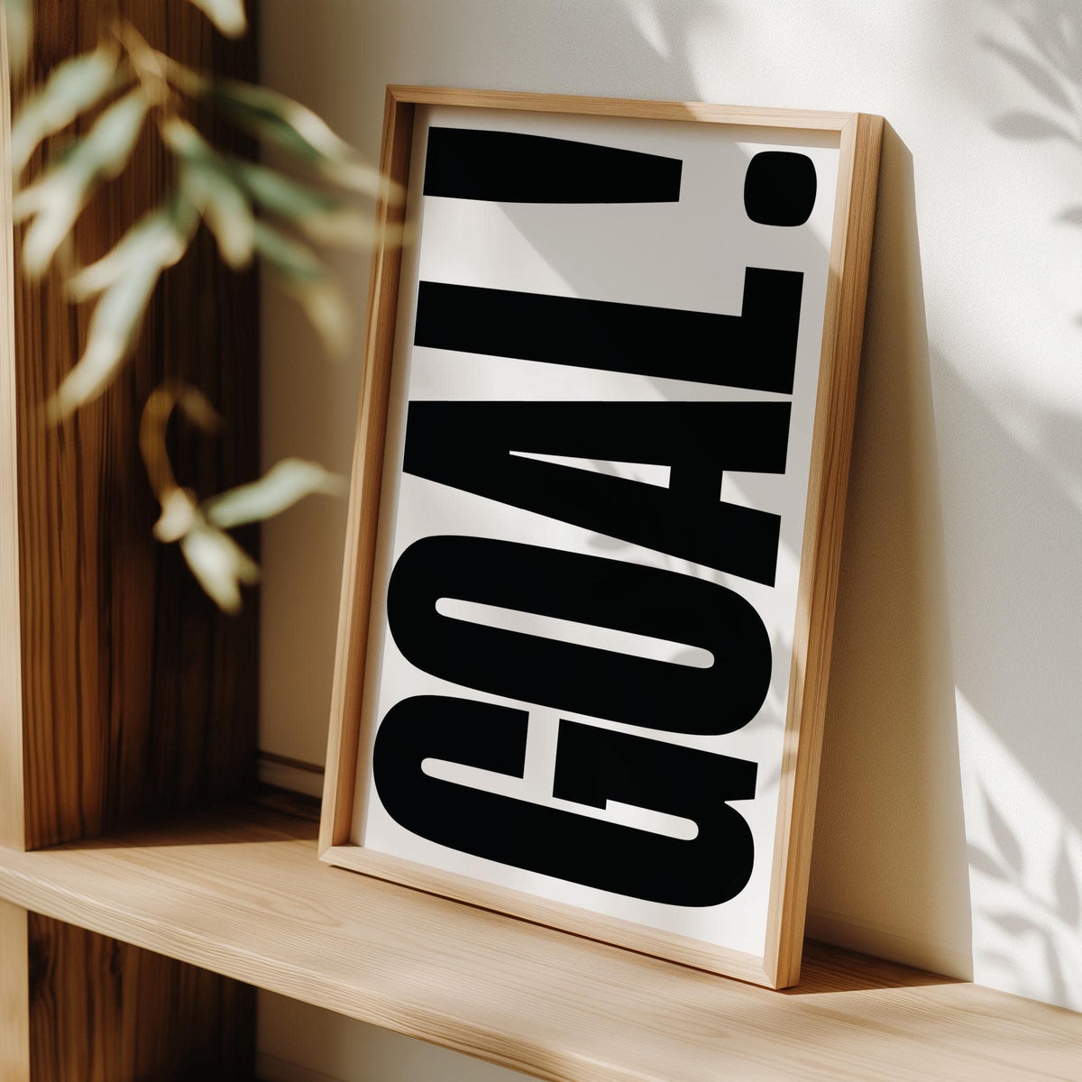 Framed print leaning on a light wood shelf with GOAL! typography in bold black letters on white background