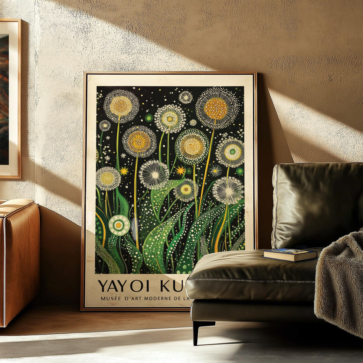 Botanical wall art of golden dandelions leaning on floor near green leather sofa with book