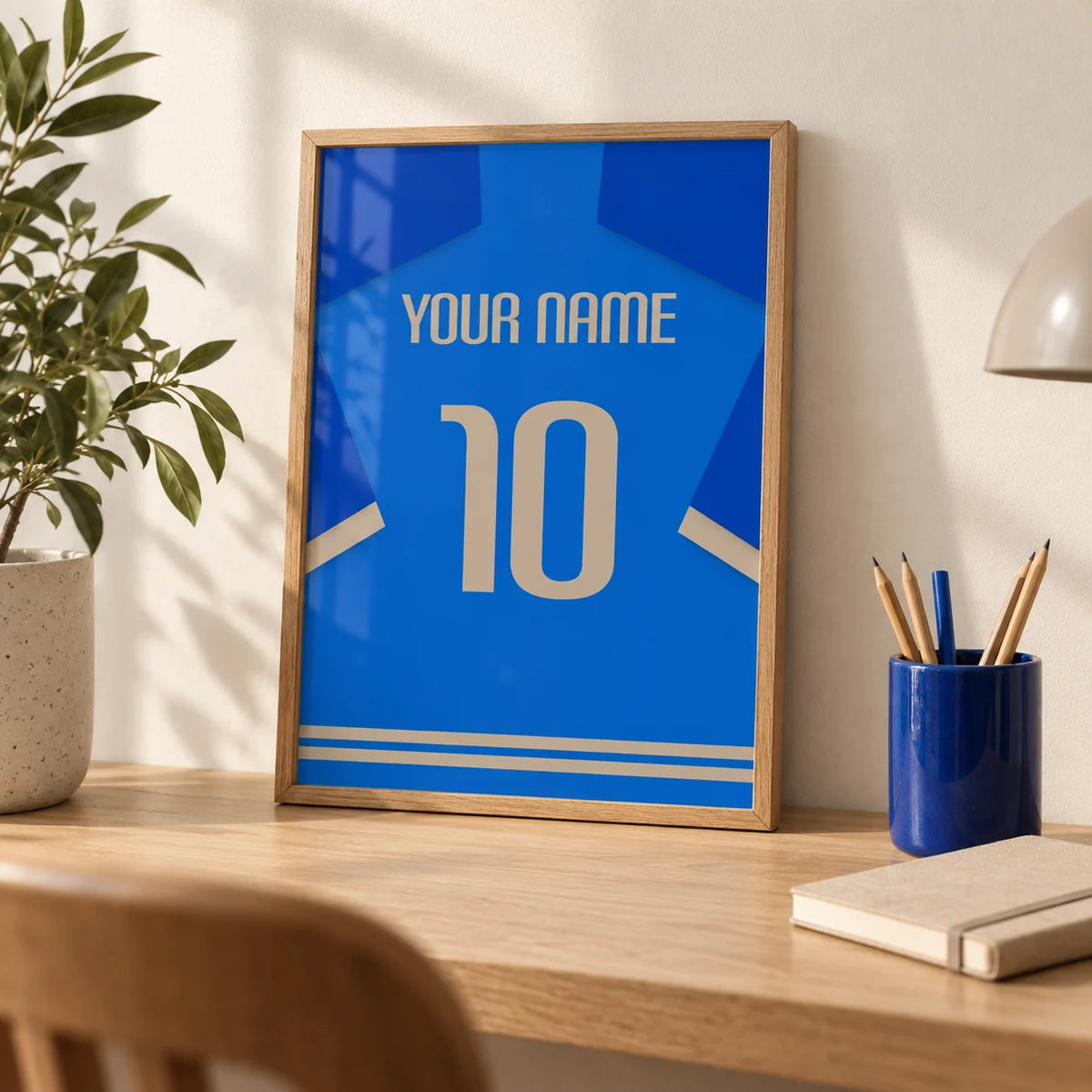 Football Shirt Poster in Blue with Beige Number, a small A4 framed print leaning on a pale oak desk