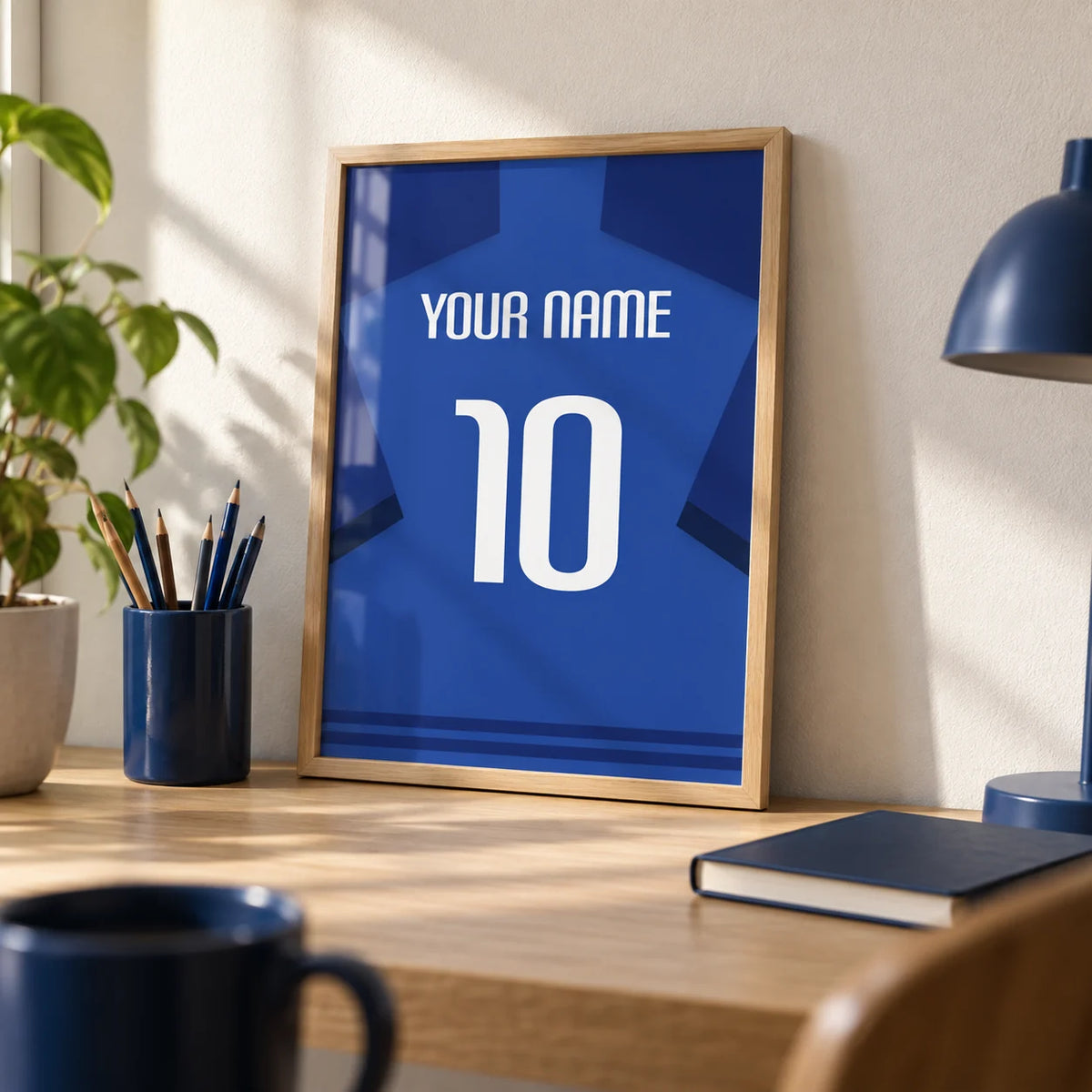 Football Shirt Poster in Blue with Dark Blue Sleeves and White Number, a small A4 framed print leaning on a pale oak desk