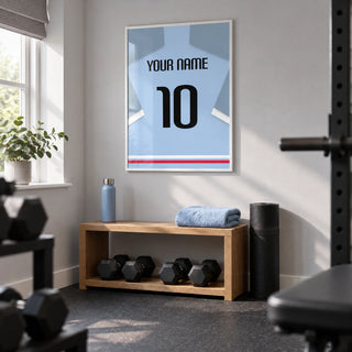 Football Shirt Poster in Light Blue with Black Number, framed on the wall of a compact home gym in a converted UK spare room with pale grey walls and dark rubber flooring