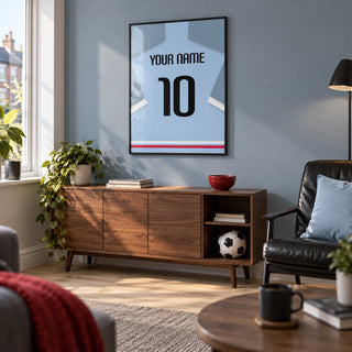 Football Shirt Poster in Light Blue with Black Number, framed on the wall of a modern football fan's snug in a UK terraced house with a muted blue-grey wall and pale oak flooring in a living room