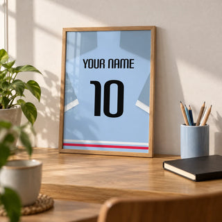 Football Shirt Poster in Light Blue with Black Number, a small A4 framed print leaning on an oak desk