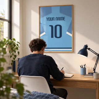 Football Shirt Poster in Light Blue with Dark Blue Number, framed on the wall of a compact home study in a young football fan's first flat (22-28) with a warm white wall