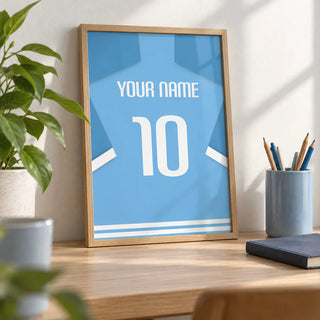 Football Shirt Poster in Light Blue with White Number, a small A4 framed print leaning on a pale oak desk
