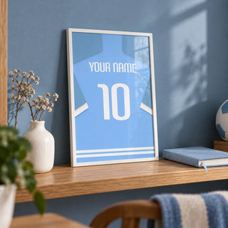 Football Shirt Poster in Light Blue with White Sleeve Stripes, a small A4 framed print leaning on an oak shelf in a home office