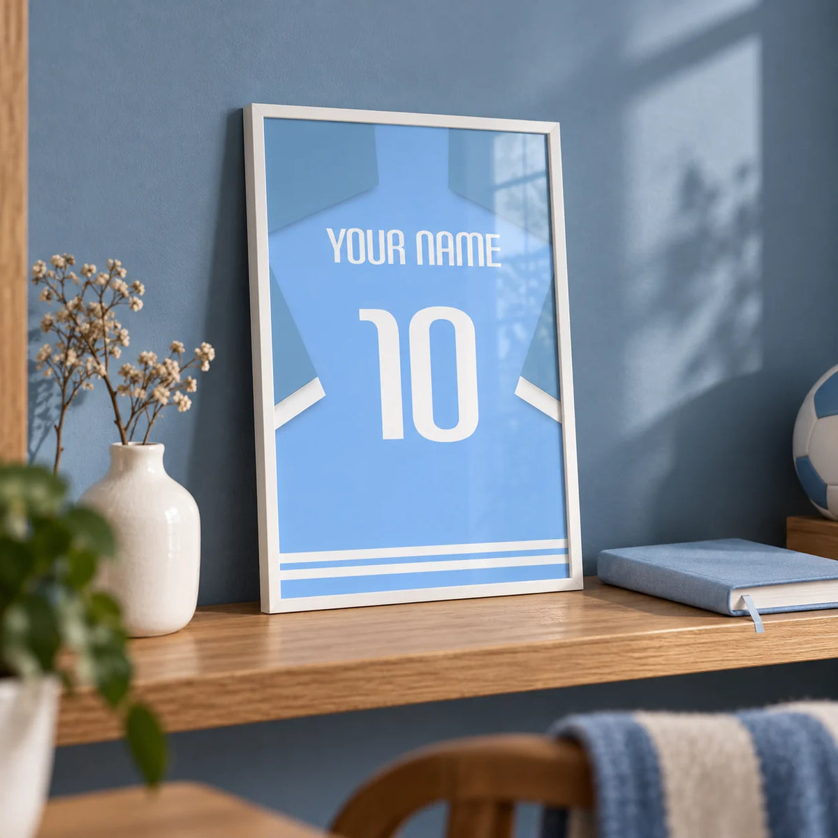 Football Shirt Poster in Light Blue with White Sleeve Stripes, a small A4 framed print leaning on an oak shelf in a home office
