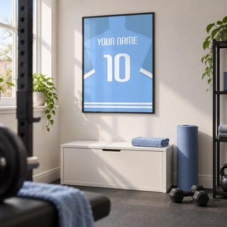 Football Shirt Poster in Light Blue with White Sleeve Stripes, framed on the wall of a tidy converted box-room home gym in a UK house with a soft white wall and plain grey rubber flooring