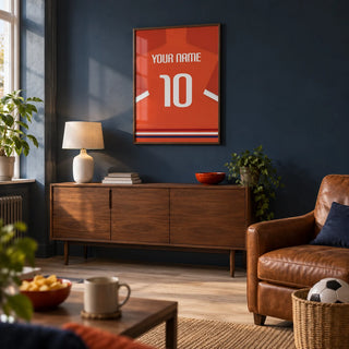 Football Shirt Poster in Orange-Red with White Number, framed on the wall of a football fan's small match-day snug in a UK terraced house with a muted navy wall and pale oak floor in a living room