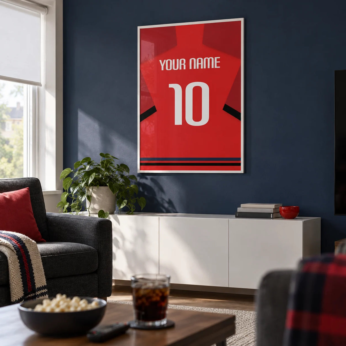 Football Shirt Poster in Red with Black Sleeve Bands, framed on the wall of a modern football-watching snug in a UK semi-detached home with a muted navy wall in a living room