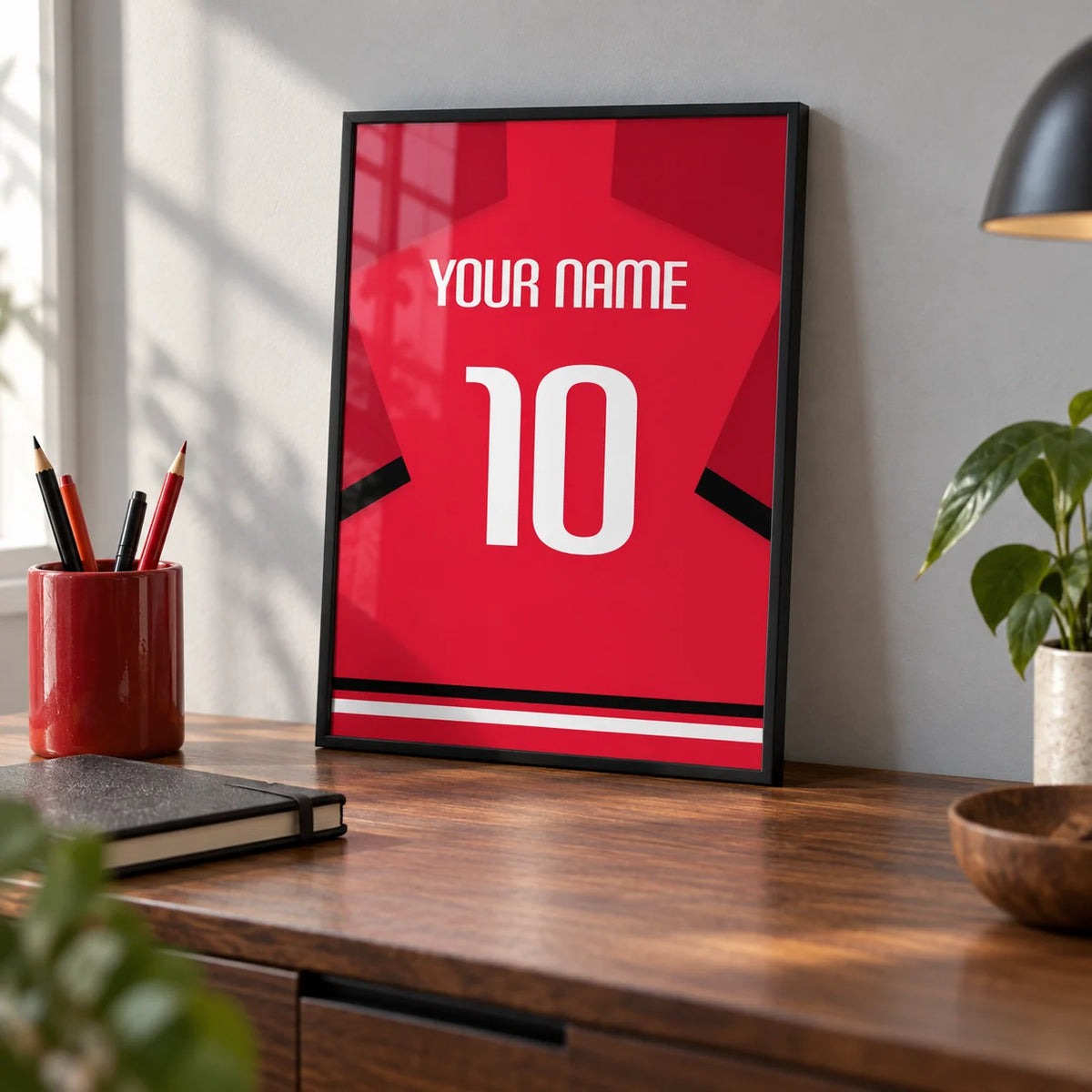 Football Shirt Poster in Red with Black Sleeve Stripe and White Number, a small A4 framed print leaning on a walnut desk