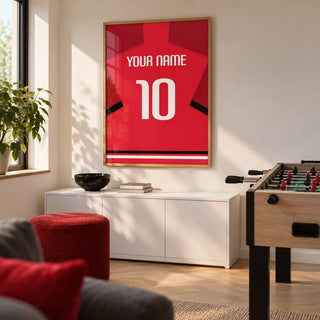 Football Shirt Poster in Red with Black Sleeve Stripe and White Number, framed on the wall of a small football-themed games room in a UK family home with a warm white wall and pale oak flooring