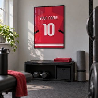 Football Shirt Poster in Red with Black Sleeve Stripe, framed on the wall of a compact home gym in a UK terraced house with a light grey wall and plain dark rubber floor