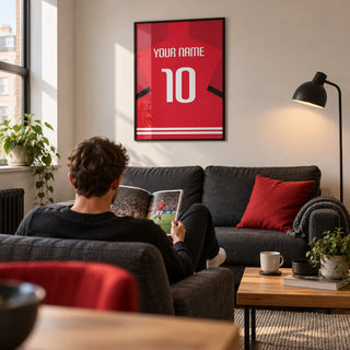 Football Shirt Poster in Red with Black Sleeve Stripe, framed on the wall of a contemporary football-viewing snug in a young adult’s UK first flat (22-28) with a warm white wall in a living room