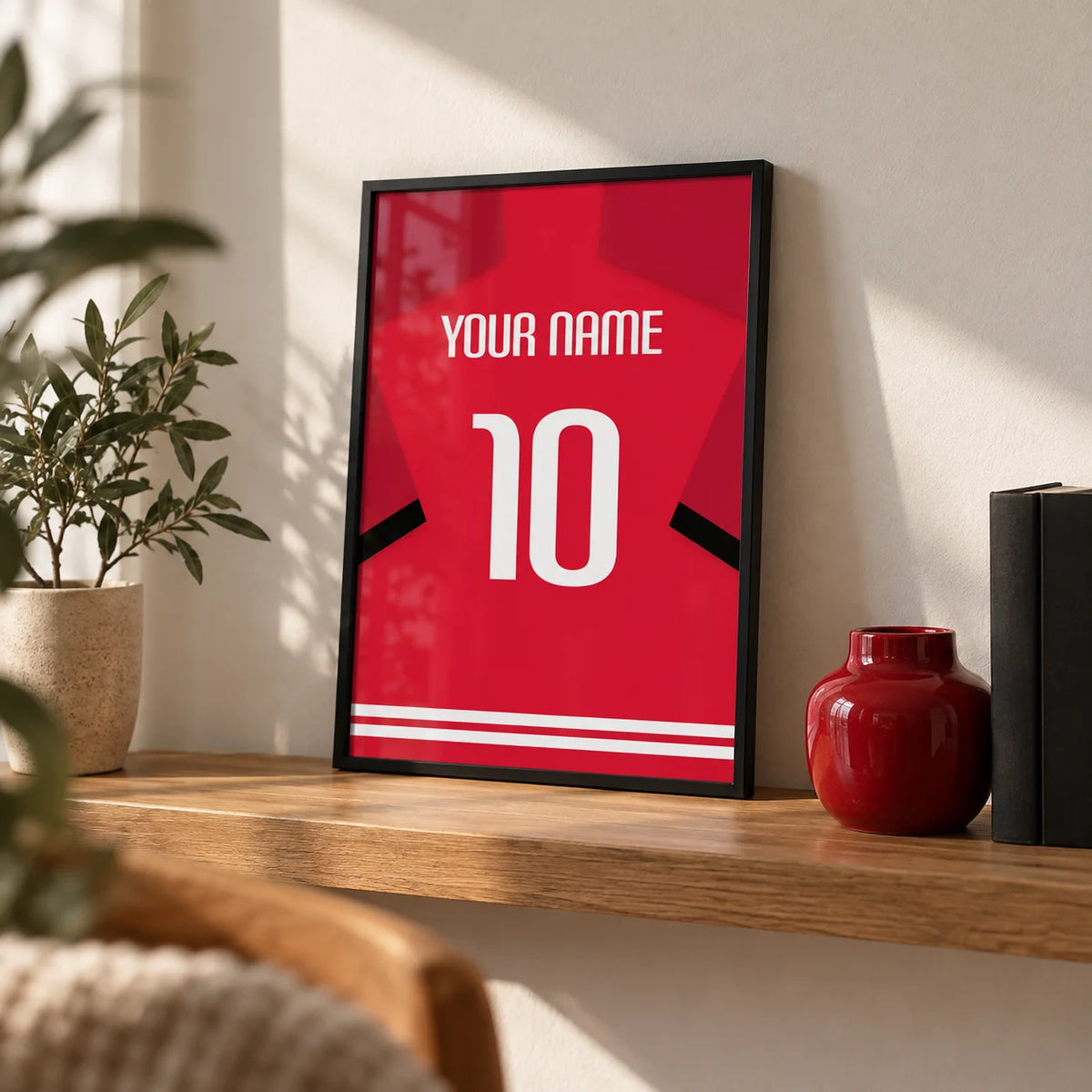 Football Shirt Poster in Red with Black Sleeve Stripe, a small A4 framed print leaning on an oak shelf in a living room
