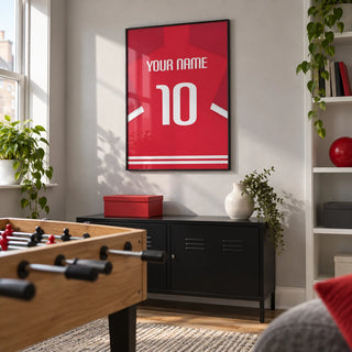Football Shirt Poster in Red with White Number, framed on the wall of a modern games room in a UK terraced house with a pale grey wall and simple white shelving
