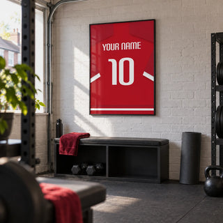Football Shirt Poster in Red with White Sleeve Stripes, framed on the wall of a modest converted-garage home gym in a UK terraced house with white painted brick and plain charcoal rubber flooring