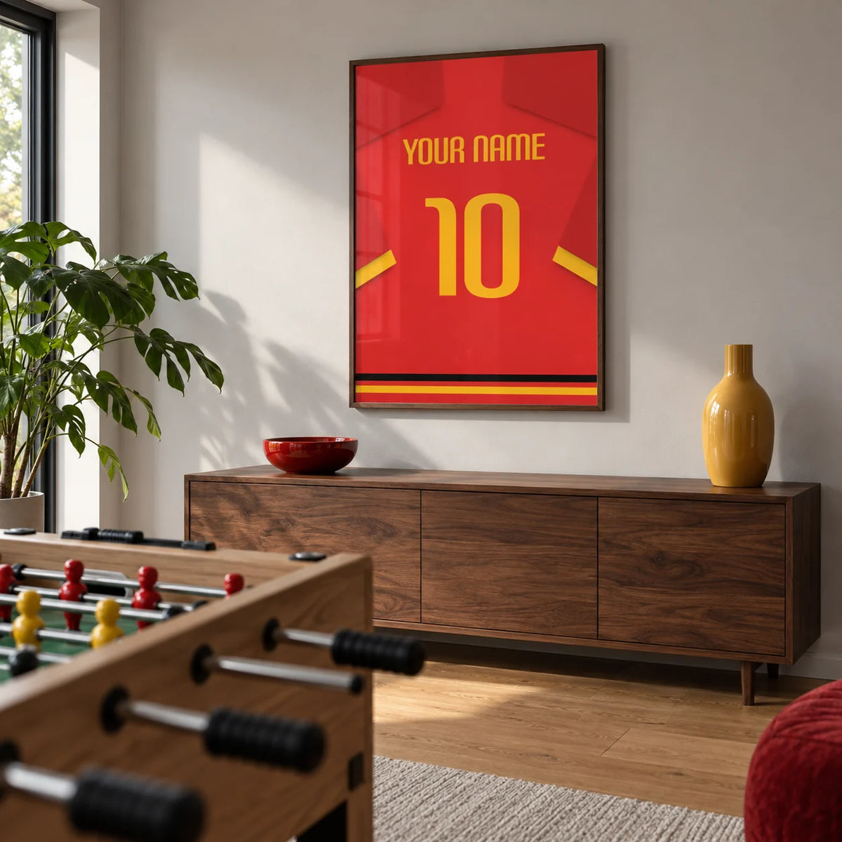 Football Shirt Poster in Red with Yellow Number and Sleeve Stripe, framed on the wall of a modern games room in a UK family home with a pale grey wall and a simple oak floor