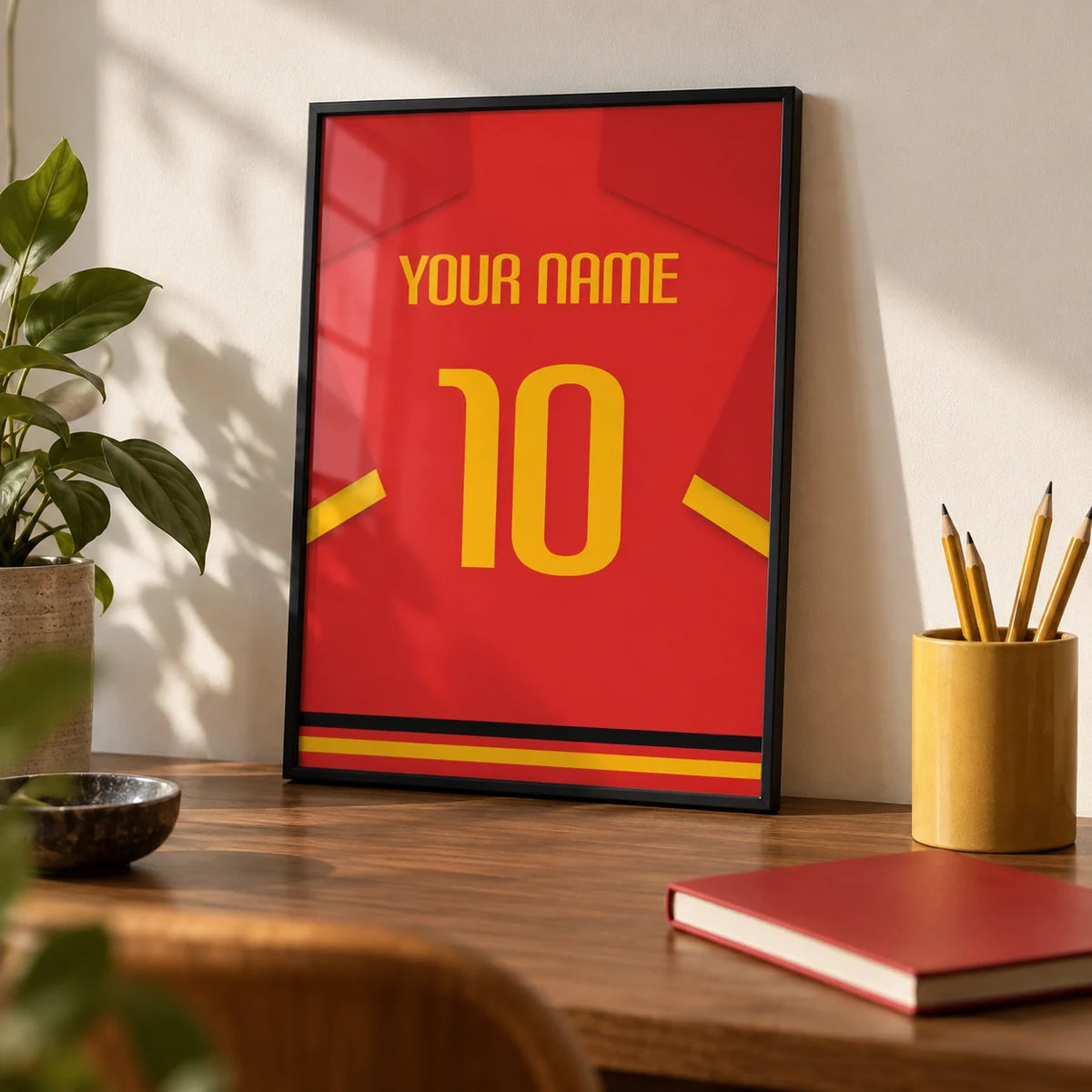 Football Shirt Poster in Red with Yellow Number and Sleeve Stripe, a small A4 framed print leaning on a walnut desk