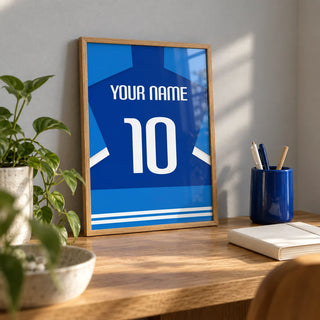 Football Shirt Poster in Two-Tone Blue with White Sleeve Stripes, a small A4 framed print leaning on an oak desk