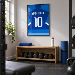 Football Shirt Poster in Two-Tone Blue with White Sleeve Stripes, framed on the wall of a small converted spare-room home gym in a UK house with a pale grey wall and dark rubber floor