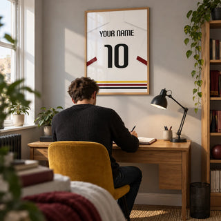 Football Shirt Poster in White with Black Red and Gold Hem Stripes, framed on the wall of a bright home study in a young adult football fan's UK terrace