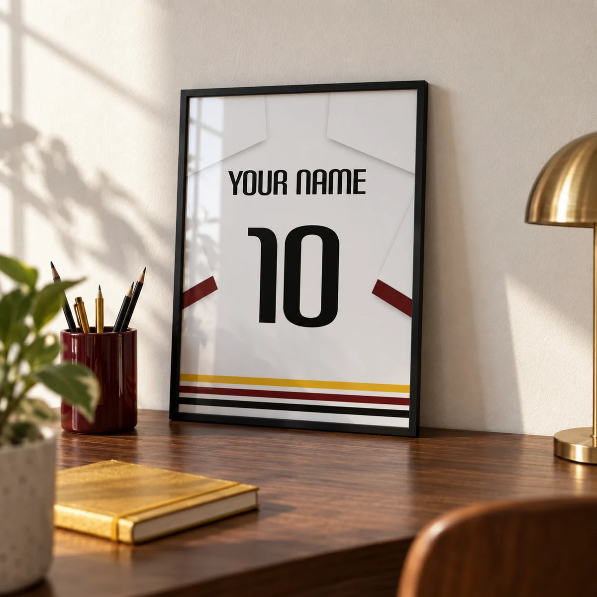 Football Shirt Poster in White with Black Red and Gold Hem Stripes, a small A4 framed print leaning on a walnut desk