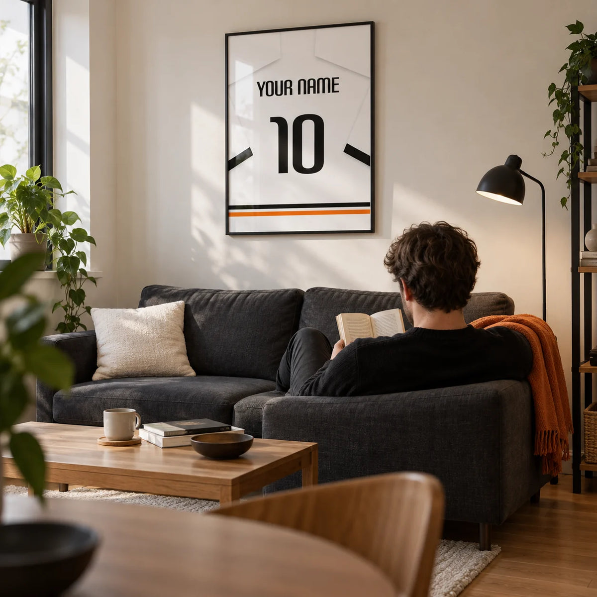 Football Shirt Poster in White with Black Sleeve Bands, framed on the wall of a compact modern living room in a football fan's first UK flat (22-28) with a warm white wall and an oak floor