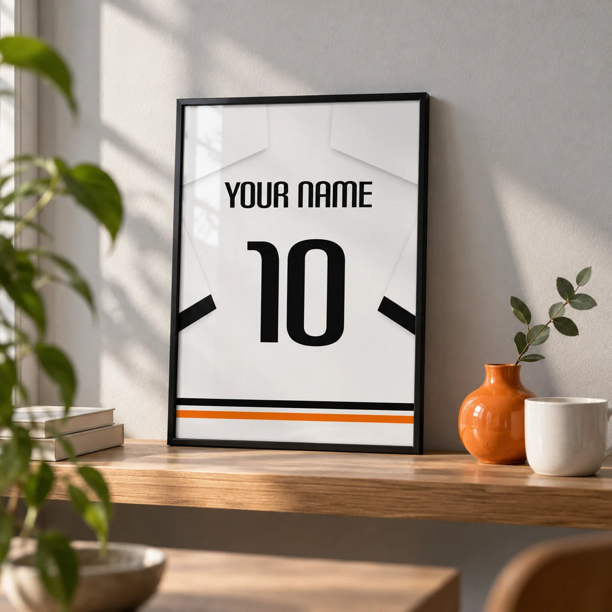 Football Shirt Poster in White with Black Sleeve Bands, a small A4 framed print leaning on an oak shelf in a living room