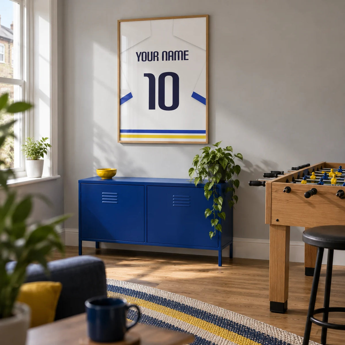 Football Shirt Poster in White with Blue Sleeves and Black Number, framed on the wall of a compact games room in a UK terraced house with a light grey wall and oak flooring