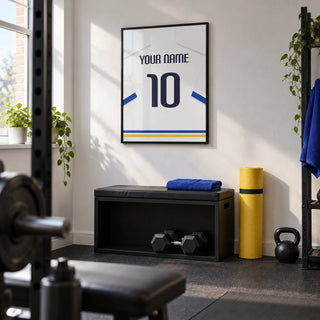 Football Shirt Poster in White with Blue Sleeves and Black Number, framed on the wall of a modest home gym in a converted UK spare room with a white wall and plain dark rubber flooring