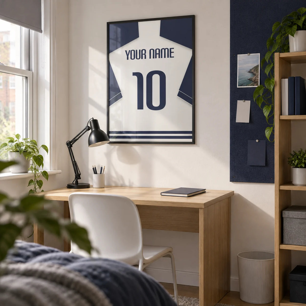 Football Shirt Poster in White with Navy Sleeves and Navy Number, framed on the wall of a compact university study corner (18-21) in a UK shared house with a white wall and a navy pinboard on the adjacent wall