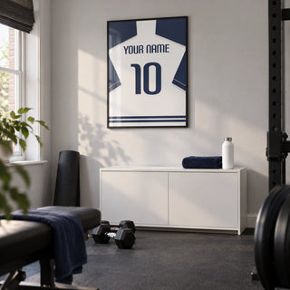 Football Shirt Poster in White with Navy Sleeves and Navy Number, framed on the wall of a modest home gym in a converted UK spare room with a pale grey wall and plain charcoal rubber flooring