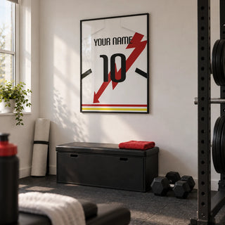 Football Shirt Poster in White with Red Lightning Bolt, framed on the wall of a modest home gym in a converted spare room in a UK house with white walls and dark rubber flooring