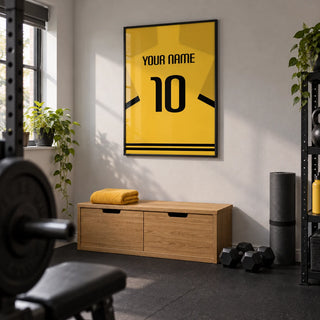 Football Shirt Poster in Yellow with Black Sleeve Stripes, framed on the wall of a compact home gym in a converted UK spare room with a light grey wall and plain black rubber floor