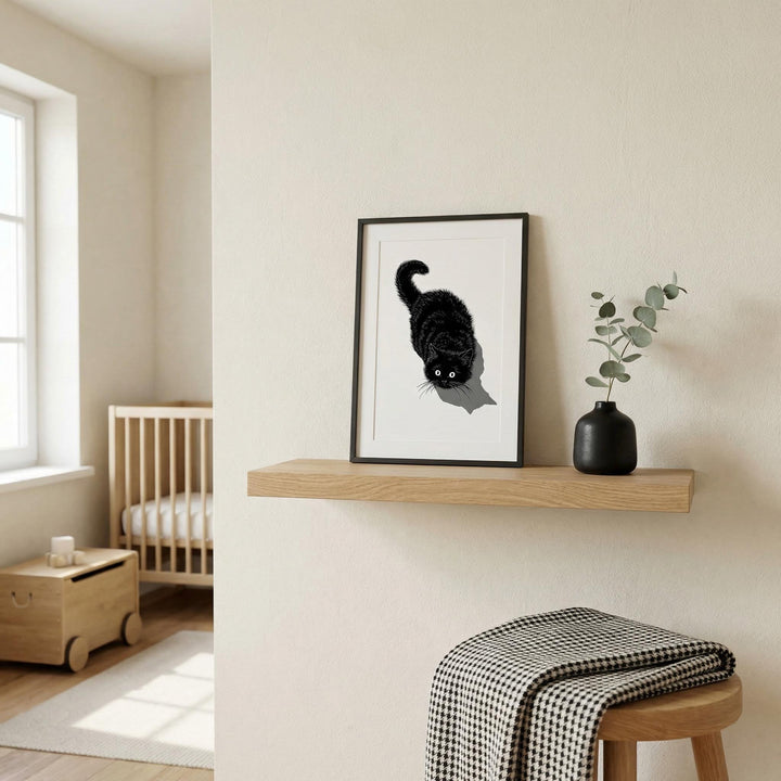 Print of a black cat looking up with shadow on a floating shelf beside a black vase with leaves in a neutral nursery