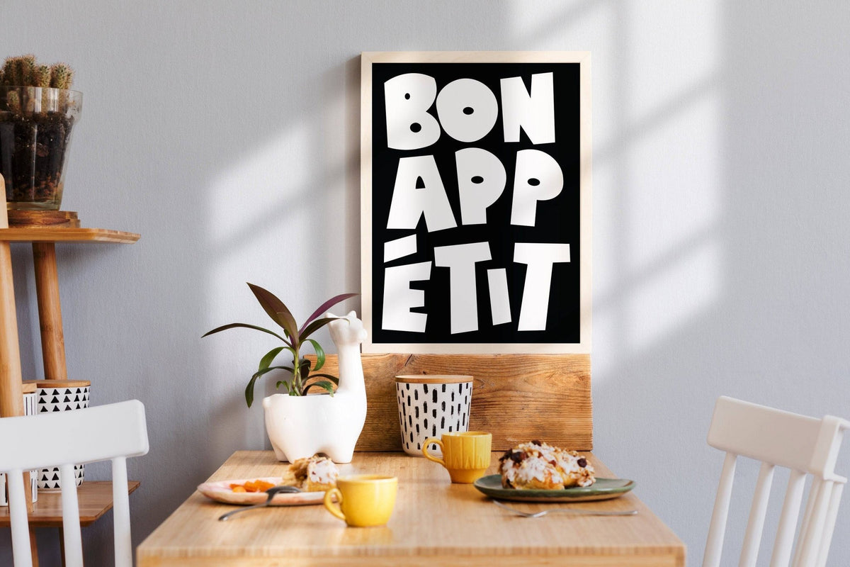 Kitchen wall art with bon appétit text in bold white on black above a wooden table with breakfast items