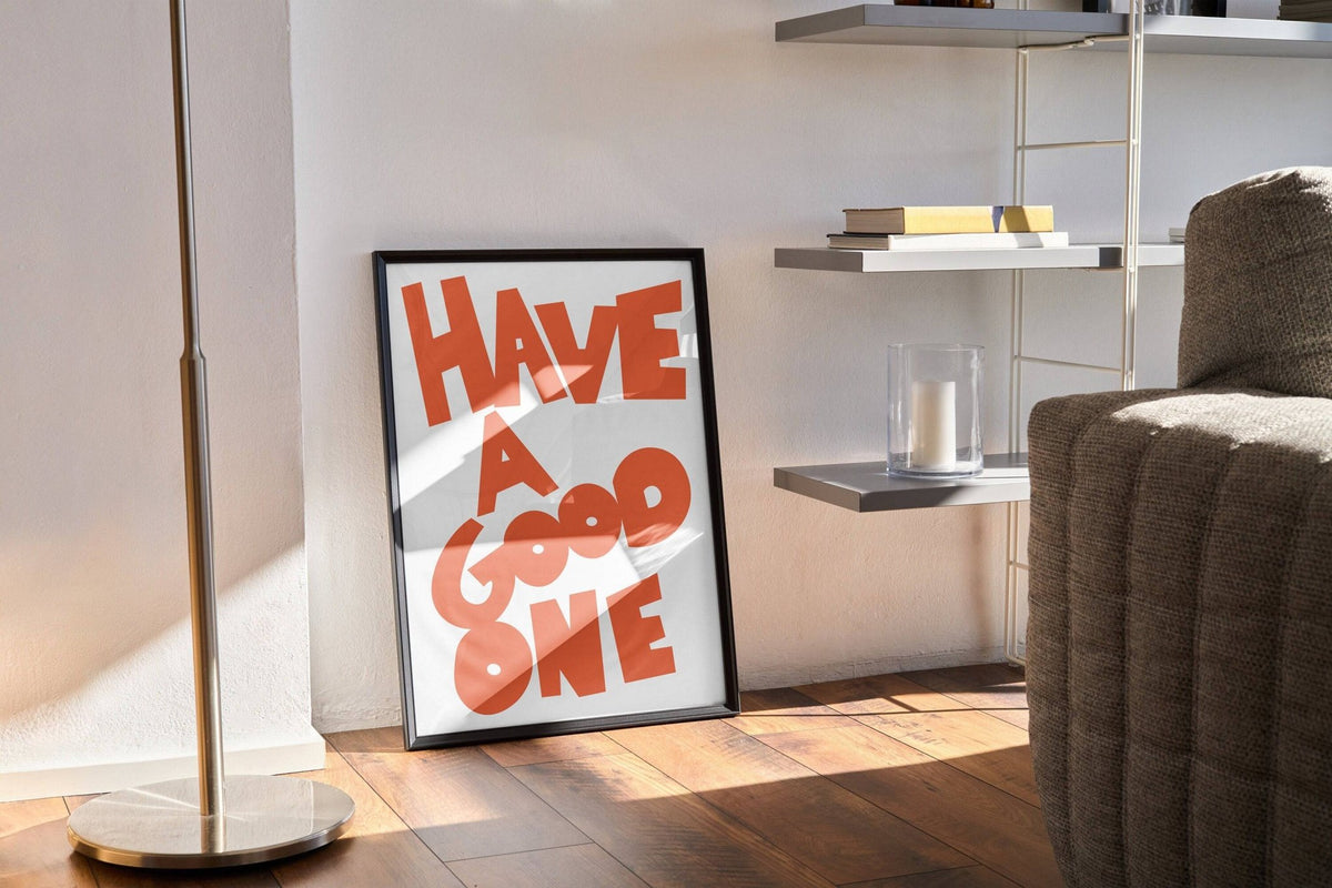 Wall Art Typography framed print with orange text leaning on the floor near a lamp and shelf