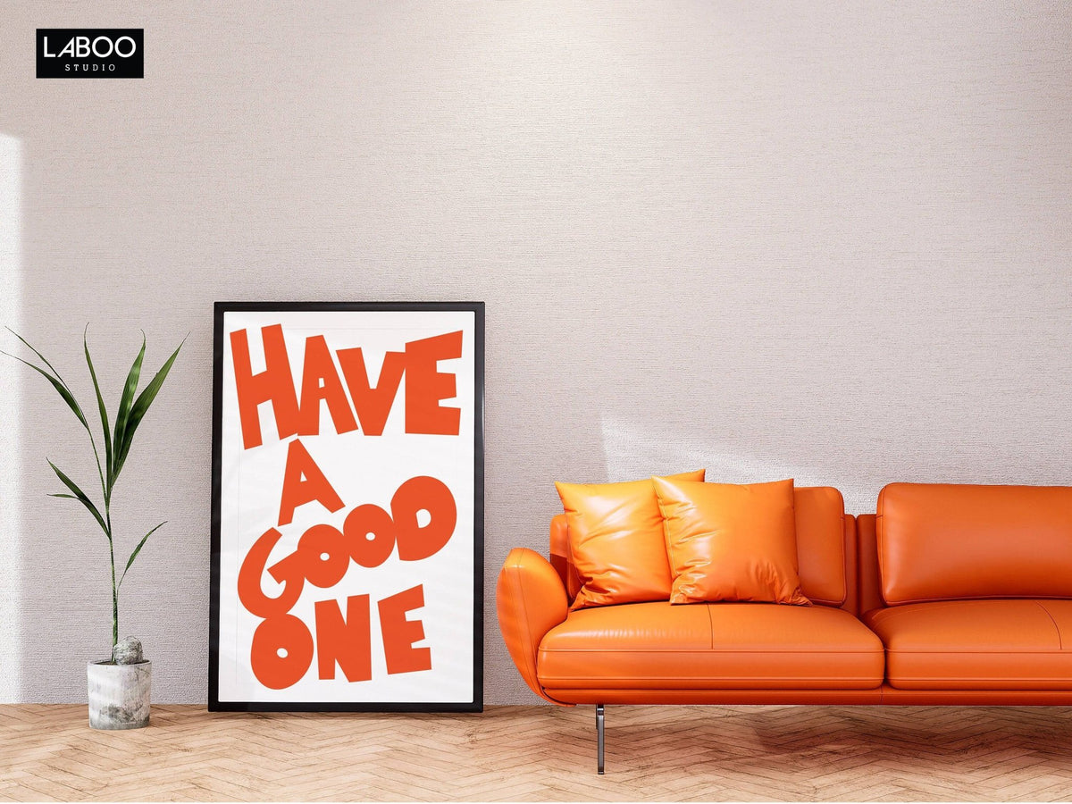 Wall art typography leaning against a light wall with orange text next to an orange leather sofa and a small plant