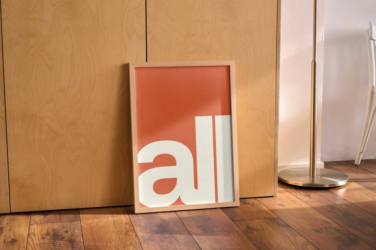Modern Typography Art print leaning on a wooden floor against wooden cabinets near a metal lamp