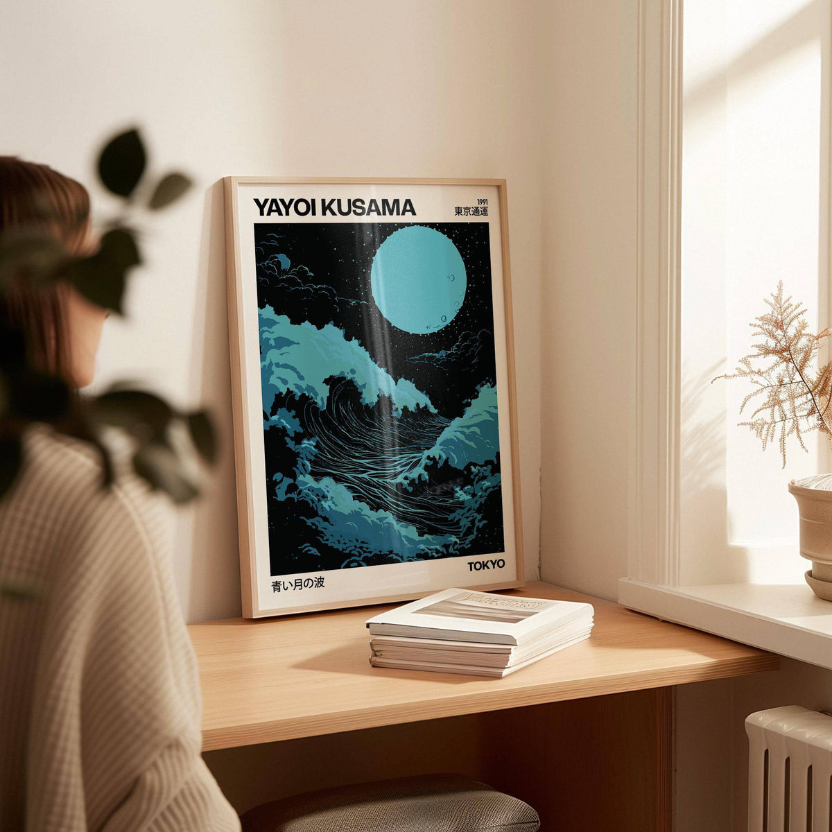 Large Ocean wall art leaning on a wooden desk with blue waves and a large moon alongside books
