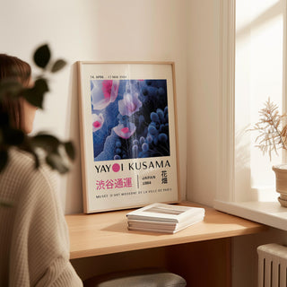 Print leaning on a shelf of purple abstract wall art with floral shapes beside a small dried plant