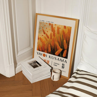 Print leaning on wooden floor showing autumnal wall art of orange wheat plants next to a stack of books and a mug